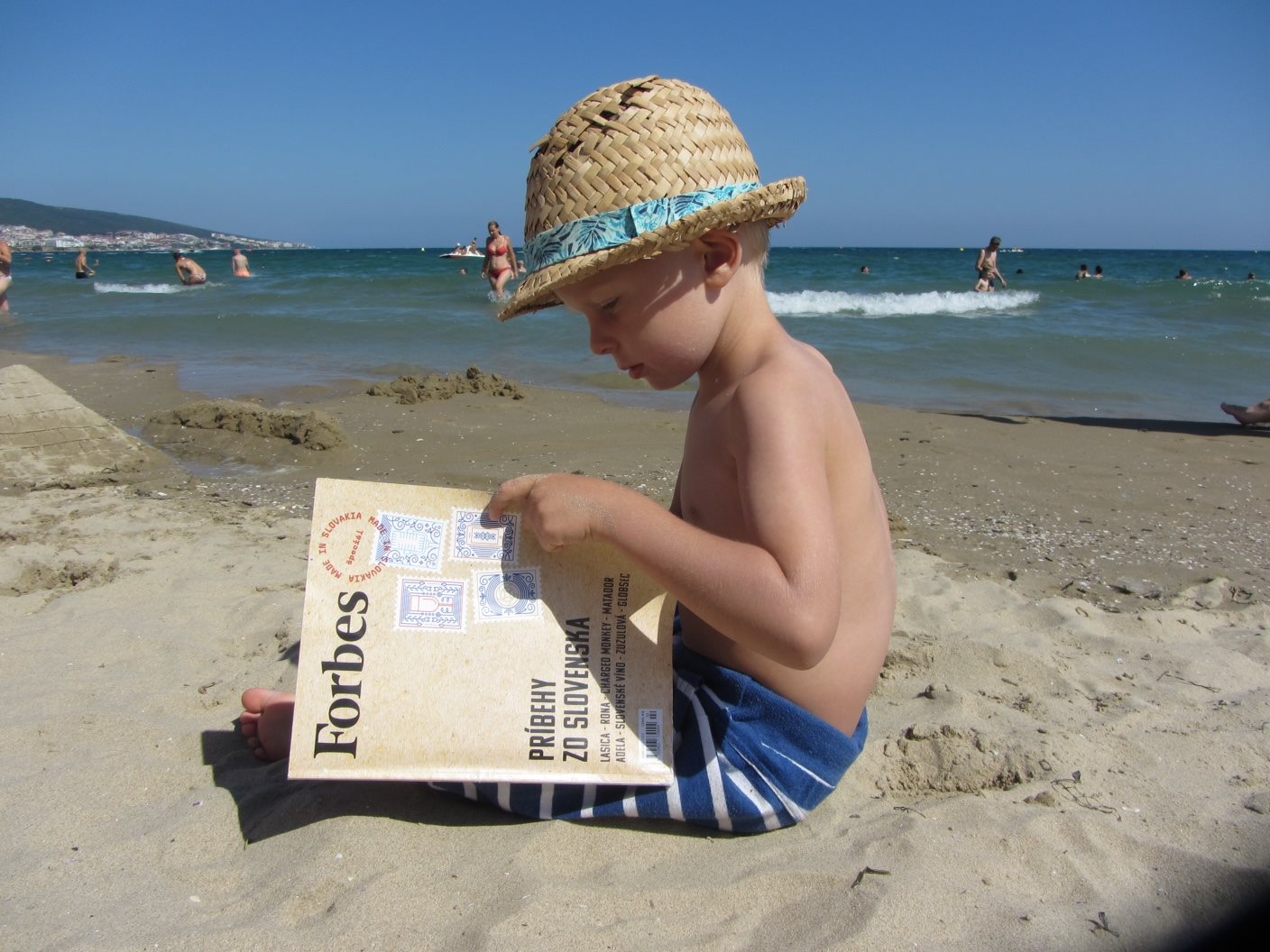 dieťa na pláži s časopisom Forbes