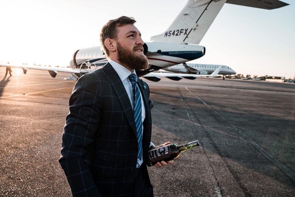 Conor McGregor oblečený v obleku drží fľašu whiskey, ktorú propaguje. 