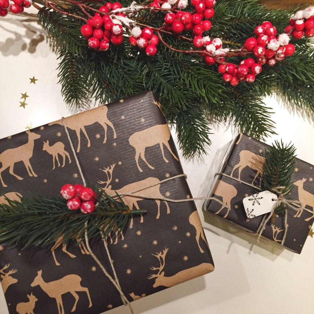 Darčeky zabalené v baliacom papieri s motívom jeleňov, previazané lankom a doplnené bobuľami a vetvičkami z ihličnatého stromu. 