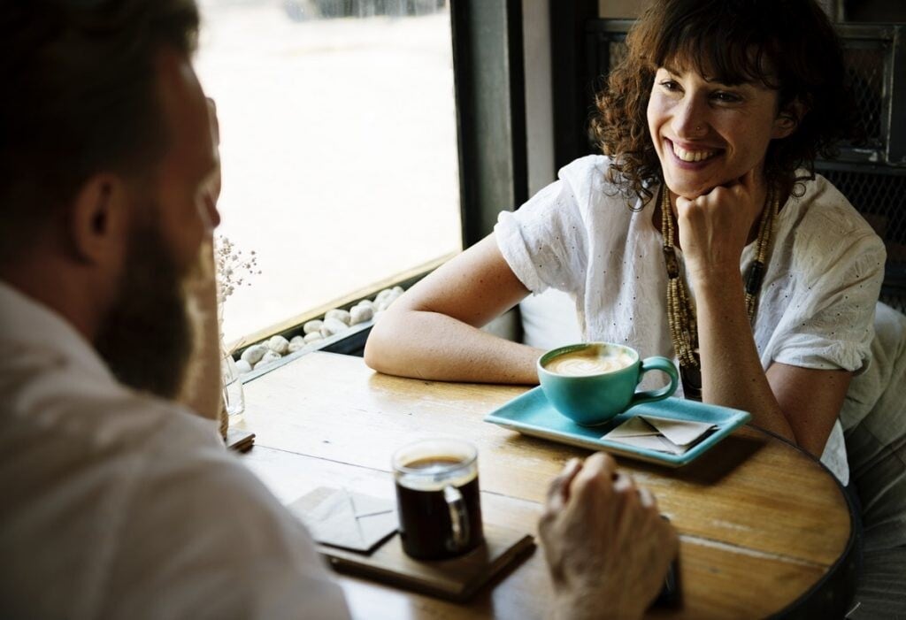 usmievajúca sa žena s mužom na káve, muž jej rozpráva príbeh 